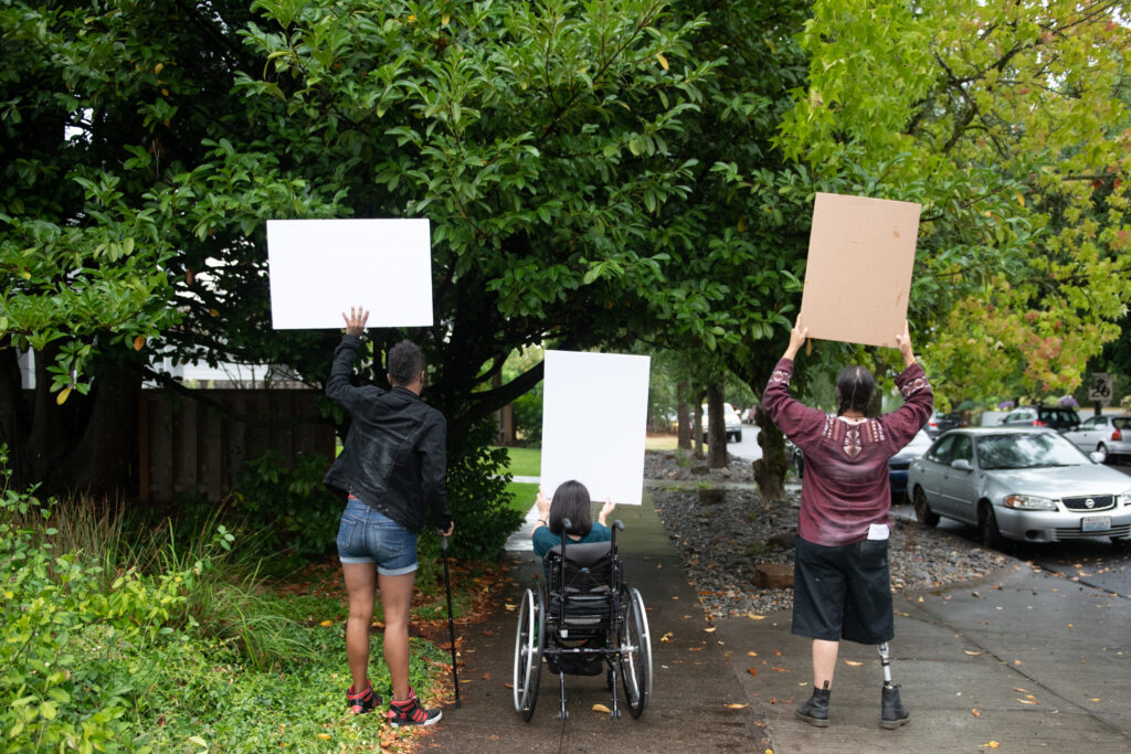 three individuals with varying abilities holding up posters advocating for themselves.